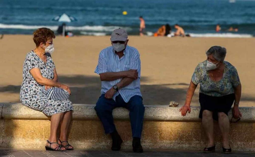 Turismo Imserso: Tres personas mayores descansan en el paseo marítimo de la playa de la Malvarrosa