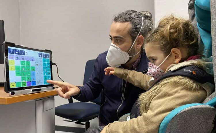 Profesional explica el uso del lector ocular a una niña pequeña con discapacidad